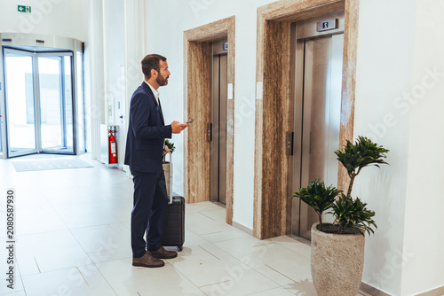 Business Traveler With Suitcase Waiting at Modern Elevator Lobby in Office Building