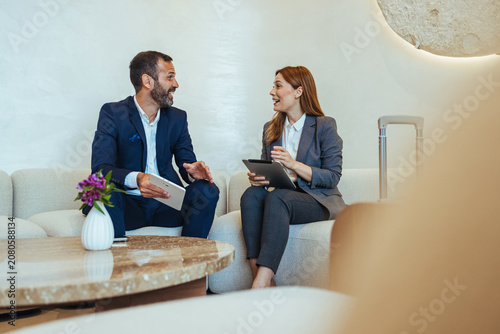 Business Colleagues Discussing Work in Hotel Lobby Lounge With Tablets and Luggage