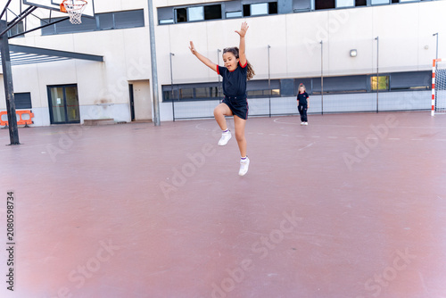 Enthusiastic young girl jumping with arms raised on an outdoor school court, expressing joy and energy during play