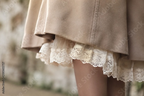Vintage lace trim peeks from under a coat hem, delicate fabric texture in soft light.