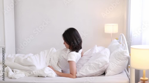 A young woman is waking up in bed (while sleeping). She is stretching her arms in the refreshing morning air, peacefully relaxing in her morning routine.