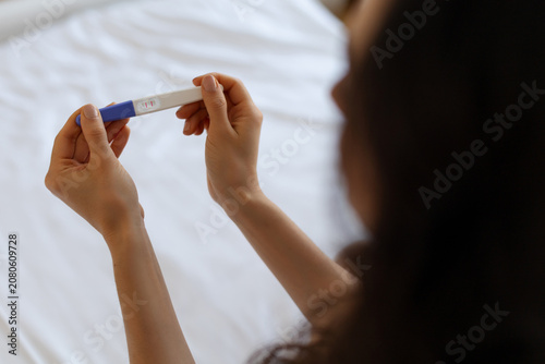 Bild auf Leinwand Closeup of young woman holding pregnancy test while sitting on bed, checking result