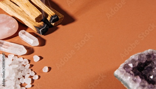 A mystical arrangement of natural elements including palo santo wood, crystals, and sea salt, set against a warm terracotta background, evoking a sense of spiritual cleansing and energy work