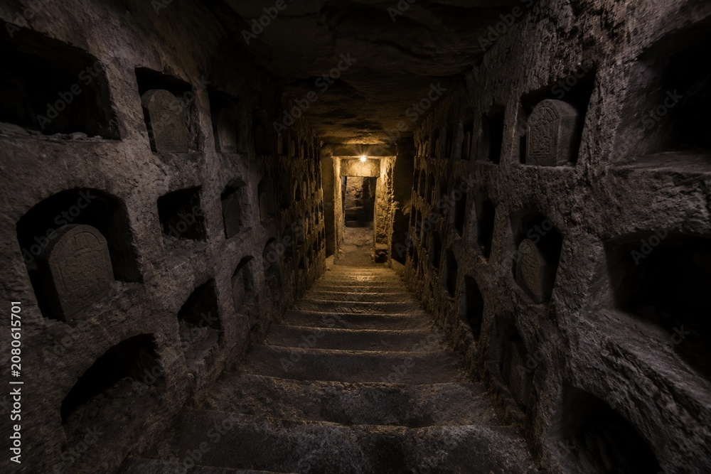 Naklejka premium Narrow stone staircase descending into dimness, burial niches lining walls.