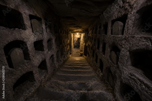 Narrow stone staircase descending into dimness, burial niches lining walls.