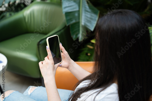 Close up of young woman holding a smartphone while viewing the screen in a modern indoor setting. Mobile photography smartphone camera and content creation for everyday photography