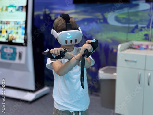 Young boy using virtual reality headset and controllers in modern gaming center
