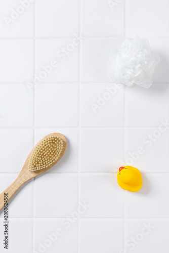 Top view of baby bath product mockup background with yellow rubber ducks. Flat lay of body brush, bath puff, and white towel on square tile wall with copy space for cosmetic display.