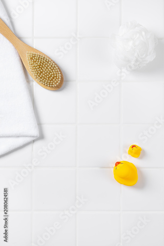 Top view of baby bath product mockup background with yellow rubber ducks. Flat lay of body brush, bath puff, and white towel on square tile wall with copy space for cosmetic display.
