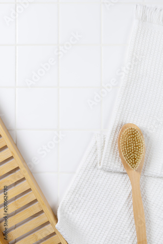 Top view of bathroom product mockup background with copy space. Flat lay of body brush, bath puff, and white towel on square tile wall for cosmetic display.