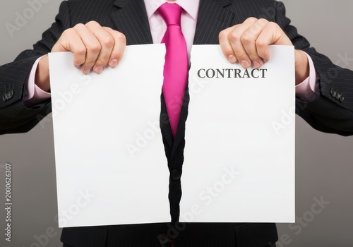 Businessman in a suit and pink tie tearing a contract document in half