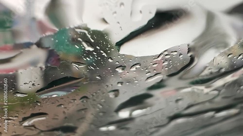 View through a rain-soaked car windshield during a downpour, with blurred traffic and water droplets creating a moody driving scene and reduced visibility