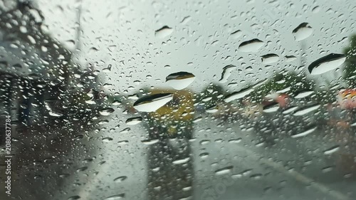 View through a rain-soaked car windshield during a downpour, with blurred traffic and water droplets creating a moody driving scene and reduced visibility