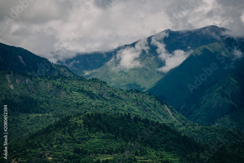 Dramatic mountain range shrouded in mist and clouds, lush green slopes contrasting with dark rock.