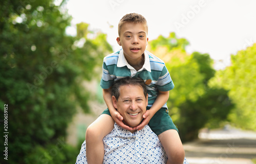 cute little child with trisomy 21 syndrome outside in summer season with his father