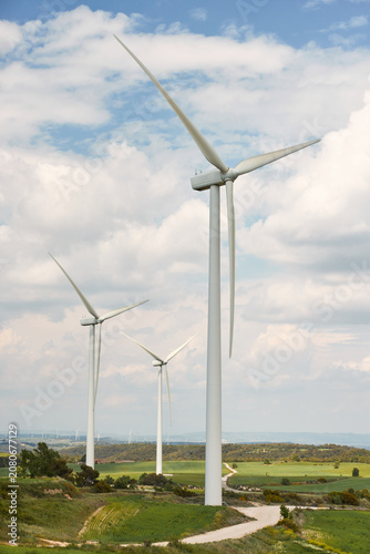 Принти на полотні Modern white wind turbines standing on lush green rolling hills under a cloudy sky, symbolizing clean renewable energy and eco-friendly technology