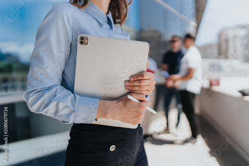 Fotografie A businesswoman holds a tablet and stylus close to her chest