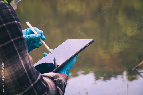 Environmental researchers collecting freshwater samples to monitor pollution and save the information on the tablet.