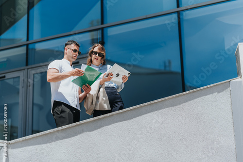 Photos Two business associates review documents and a tablet while standing on an office balcony
