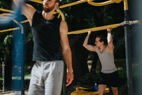 Canvas Print Two men perform pull-ups on yellow monkey bars in an outdoor park