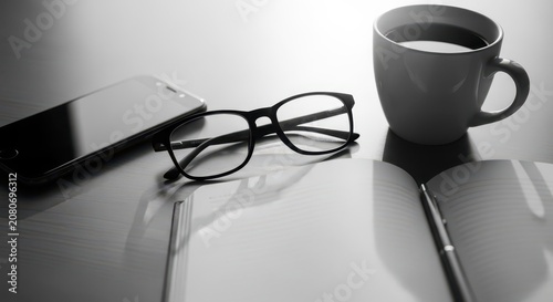 Black framed eyeglasses resting beside a coffee cup and notebook on a reflective desk surface, suggesting a productive work or study session.