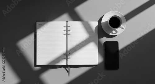 Open blank notebook with coffee and smartphone on a table with dramatic light and shadows
