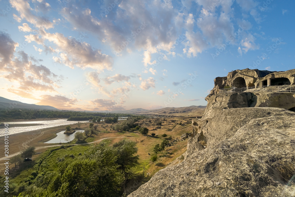 Fototapeta premium Georgian landscape with Kura river sunset sky with cloud and famous Uplistsikhe cave town in Georgia