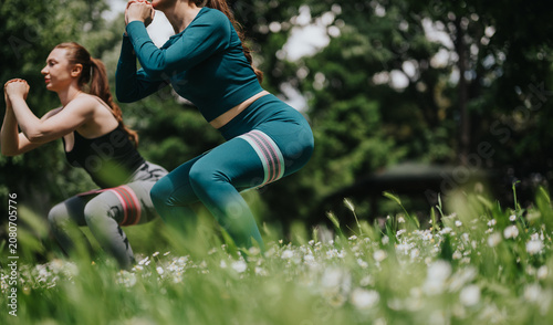 Canvastavla Two women perform squats with resistance bands while exercising outdoors