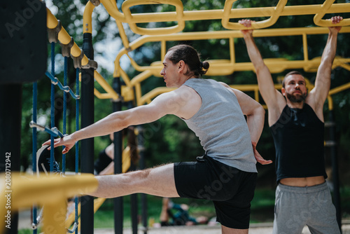 Photography Two men perform stretches and bodyweight exercises on yellow monkey bars outdoors