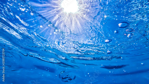 Underwater view looking up toward the surface with the sky, sun and rays of sun shinning through and bubbles floating upward 