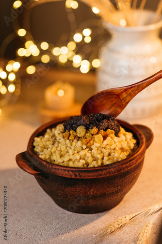 Traditional Ukrainian Christmas dish Kutia made of wheat berries, poppy seeds, and raisins served in a clay bowl with a wooden spoon