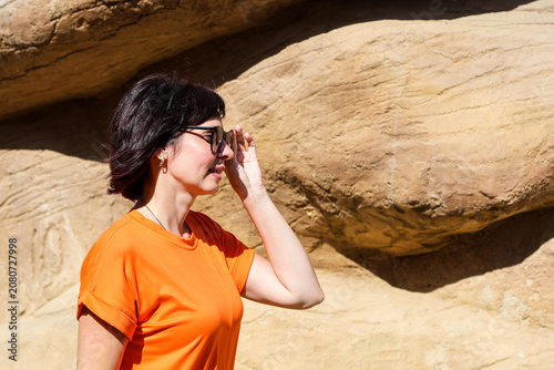 Young woman in a short summer orange dress and sunglasses enjoying sunny day outdoors, radiating joy and vibrant summer vibes.
