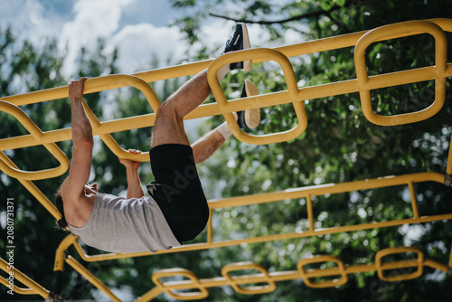 Photography Young man hangs from yellow monkey bars performing a bodyweight exercise in an outdoor park