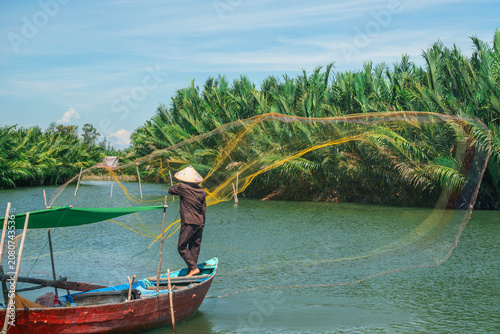 Vietnamese fisherman casting a large yellow net from a traditional wooden boat