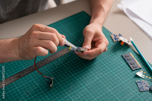 Valokuva A person uses a tool to work on a circuit board at a desk