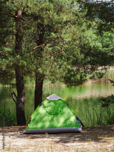 green camping tent in the pine forest near the lake in summer