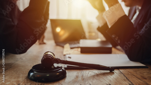 Fotografie The lawyer sat in front of a laptop in a room filled with documents and smartphones, with a hammer and scales beside him, advising his female client on matters of justice and legal principles