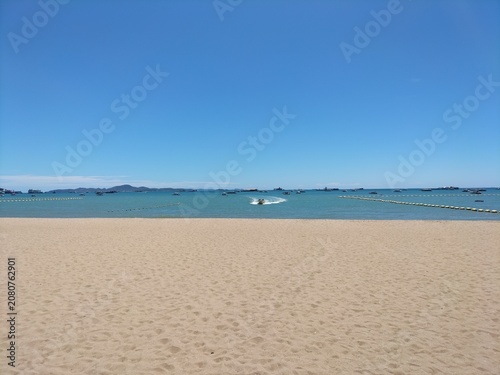 Beautiful tropical beach with golden sand, clear blue sea and sky, speed boat running in the distance.
