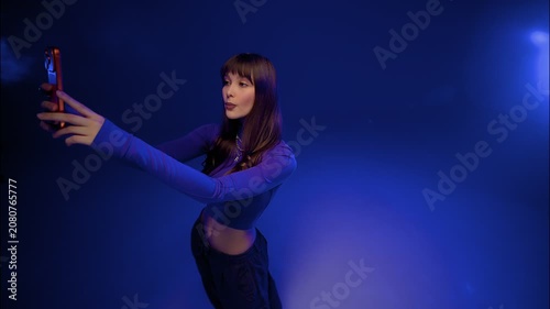 Focused young woman posing with smartphone in blue violet studio light against dark backdrop scene