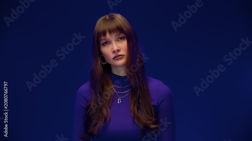 Young Woman Shifting From Neutral Gaze To Soft Smile In Studio With Blue Background And Purple Top
