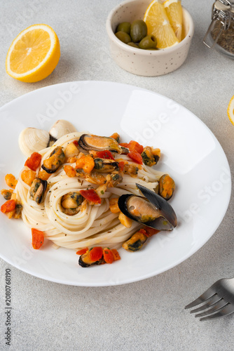 Italian pasta with mussels and tomatoes served on a white ceramic plate, with lemon slices and olives on a bright background