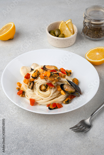 Italian pasta with mussels and tomatoes served on a white ceramic plate, with lemon slices and olives on a bright background