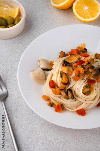 Italian pasta with mussels and tomatoes served on a white ceramic plate, with lemon slices and olives on a bright background