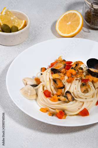 Italian pasta with mussels and tomatoes served on a white ceramic plate, with lemon slices and olives on a bright background