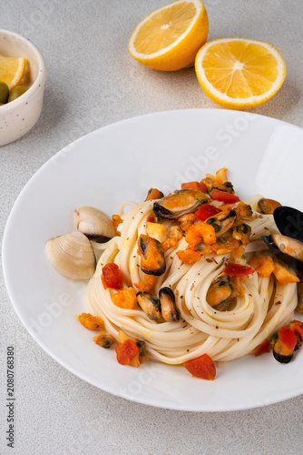 Italian pasta with mussels and tomatoes served on a white ceramic plate, with lemon slices and olives on a bright background