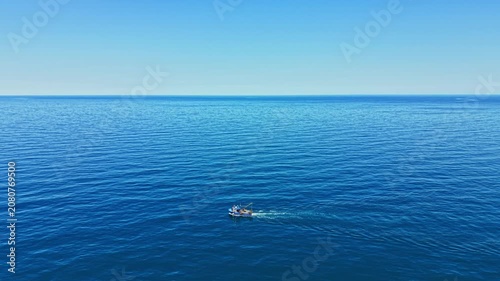 A small boat travels across the blue ocean water under a clear sky during midday. The scene shows wide water with gentle waves. It captures the simple joy of being on the water.
