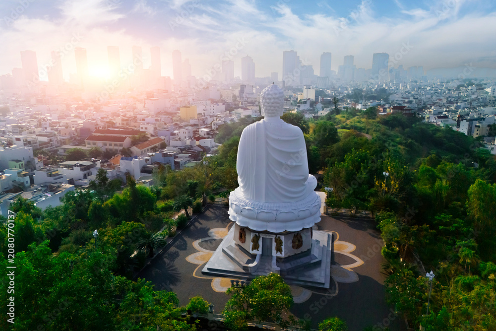 Fototapeta premium White Buddha atop Long Son Pagoda hill watches Nha Trang city awaken at sunrise, warm light painting the urban scene and lush trees