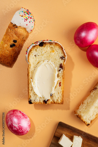 Traditional Easter sweet bread Paska slice spread with creamy butter, served with pink dyed eggs on a peach background