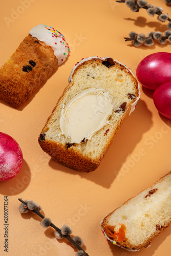 Traditional Easter sweet bread Paska slice spread with creamy butter, served with pink dyed eggs on a peach background