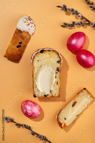 Traditional Easter sweet bread Paska slice spread with creamy butter, served with pink dyed eggs on a peach background